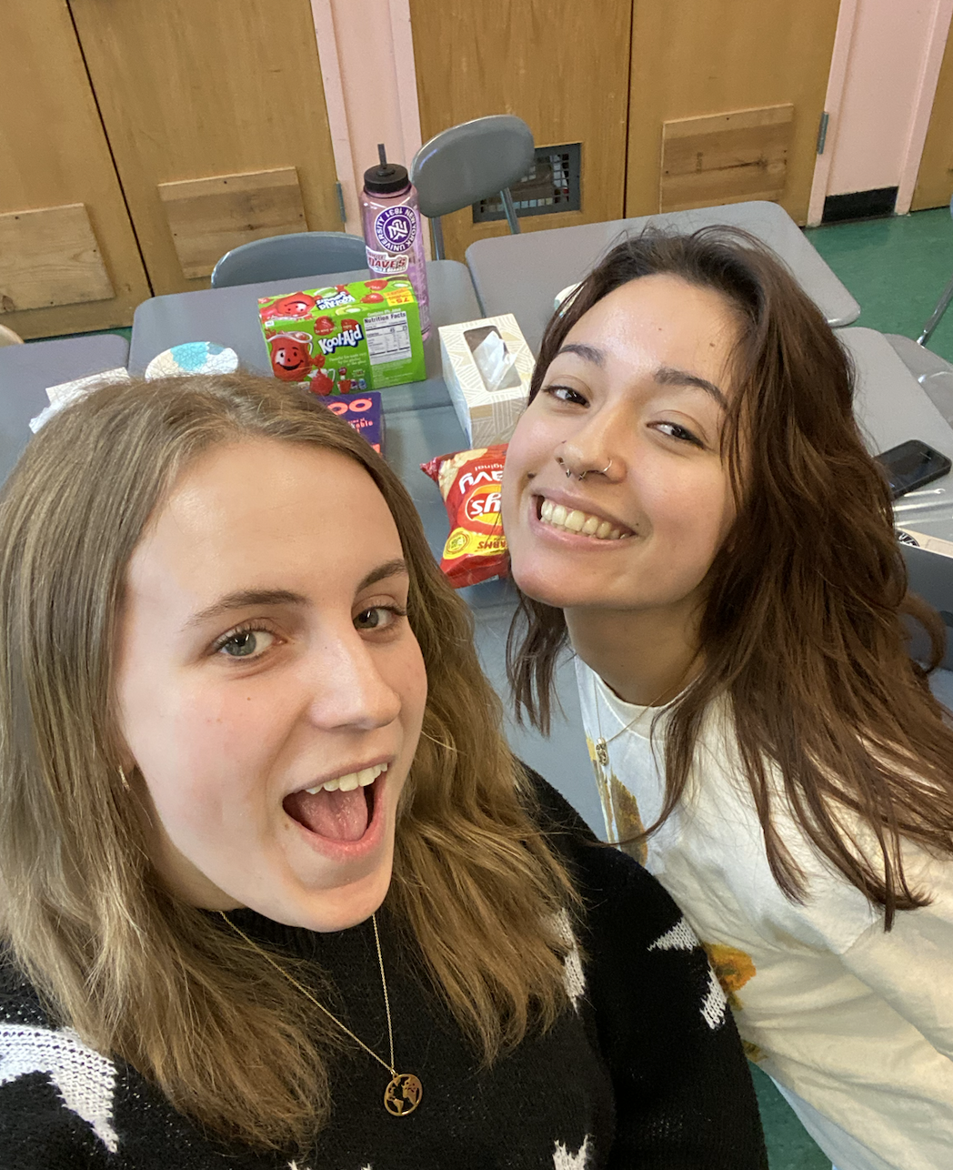 Two female-presenting NYU Social Work majors smile in front of a table with snacks on it.